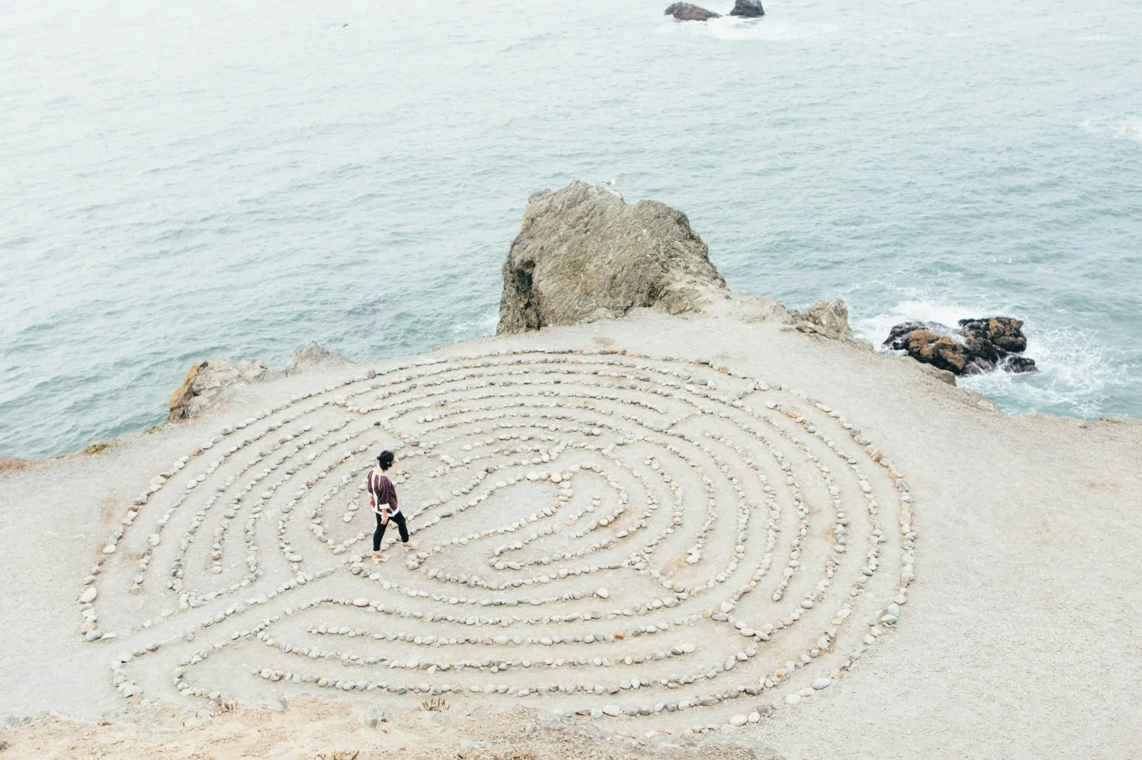 A person walking a stone labyrinth beside the sea