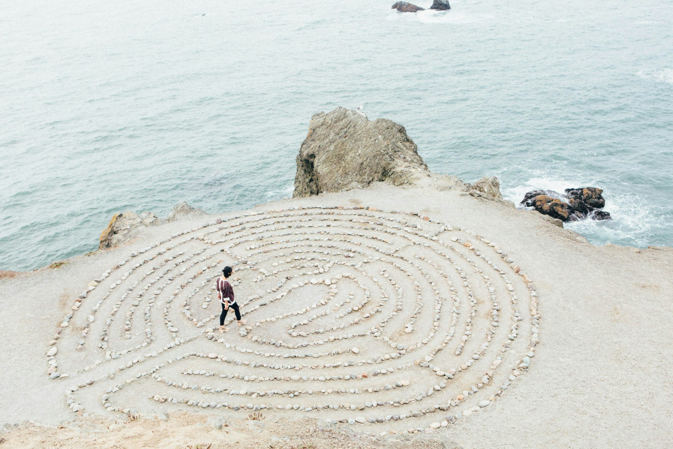 A person walking a stone labyrinth on a sunlit headland by the sea