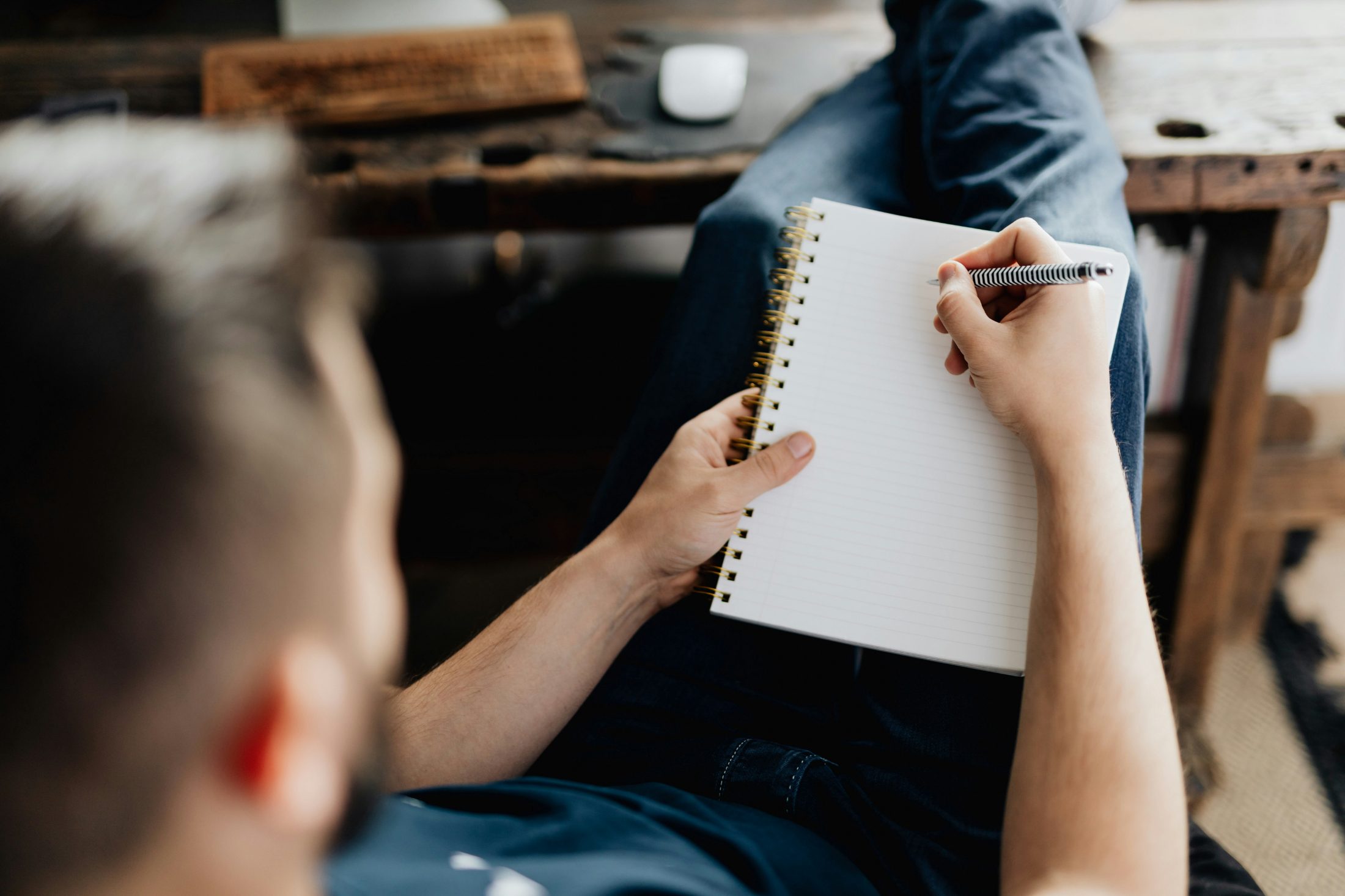 A man writing in a notebook at a wooden table
